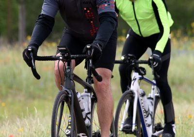 Vibrant cycling imagery of two men riding bikes outdoors in casual sportwear, wearing helmets and sunglasses, during daytime.
