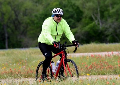 High-visibility cyclist on a scenic trail during daytime, promoting Bluebonnet Express bike services.