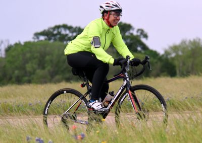 Bright safety cyclist on mountain bike riding through grassy field during daytime.