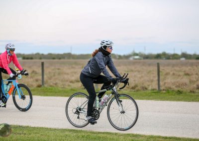 Bright female cyclist riding on a paved trail during daytime in Texas, promoting Bluebonnet Express bike service.