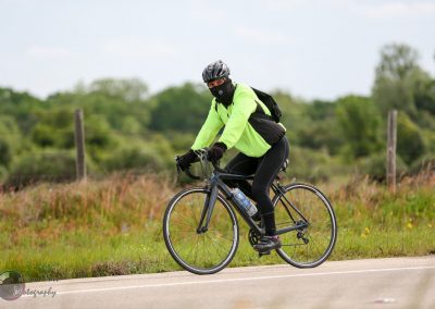 Bright neon cycling jacket on a cyclist riding on scenic country road during daytime.
