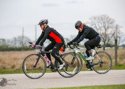 Brightly colored women enjoying a scenic bike ride outdoors on road bikes.