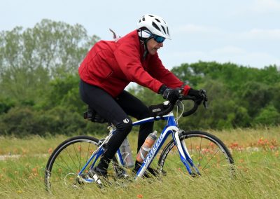 Vast outdoor riding scene with cyclist in red jacket on blue Specialized bike in grassy field.