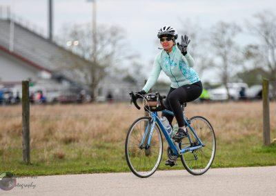 Bright woman cyclist waving while cycling on a scenic trail, promoting Bluebonnet Express bike rides and outdoor fitness.