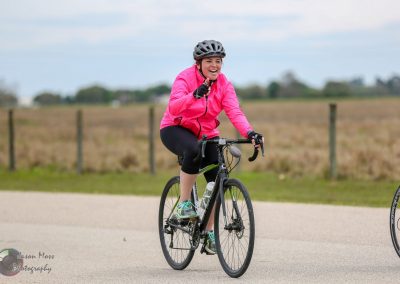Vibrant woman cycling outdoors in pink jacket, enjoying a scenic ride on a sunny day.