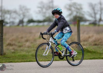 Child cyclist riding a bike at Bluebonnet Express event, wearing helmet and race bib.
