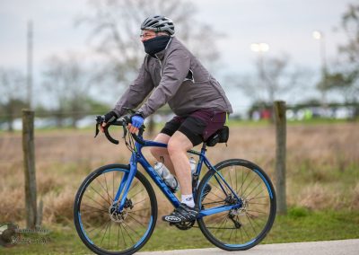 Comfortable cyclist riding Bluebonnet Express e-bike on paved trail in outdoor park setting.