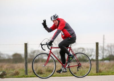 Joyful cyclist riding a red bike outdoors, showing peace sign and smiling.