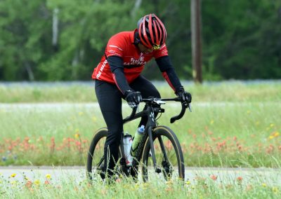 Bright red helmet and jersey on cyclist riding through scenic countryside with wildflowers, promoting Bluebonnet Express cycling event.