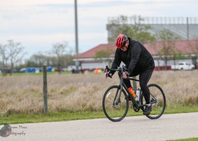 Cyclist riding a black road bike outdoors during daytime, emphasizing Bluebonnet Express cycling event.