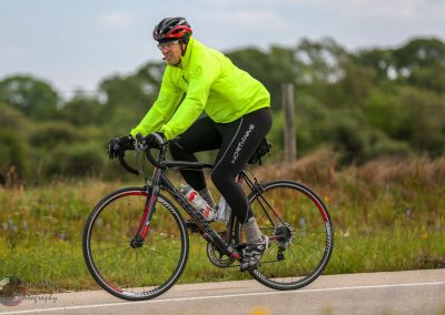 Vibrant cyclist in neon yellow jacket riding a bike on scenic countryside road.