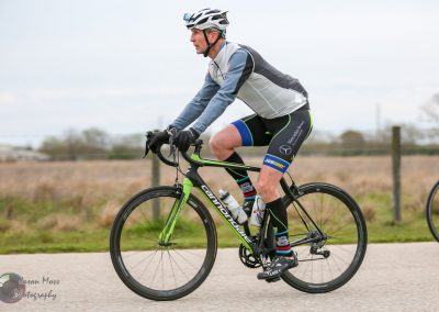 High-performance cyclist riding a green Cannondale bike on a paved trail, wearing a helmet and athletic gear.