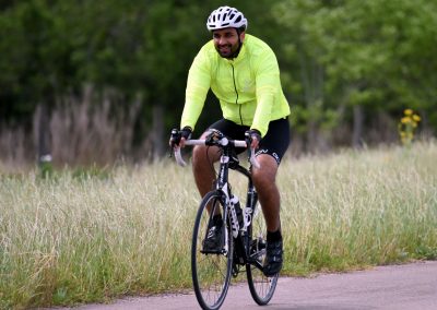 Men riding a bicycle on a scenic trail during daytime, wearing a bright yellow jacket and helmet.