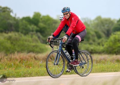 Vegan man cycling outdoors on a scenic trail with lush greenery and colorful wildflowers.