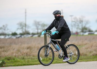 Bright blue gloves on cyclist riding mountain bike on paved trail, outdoor park scene.