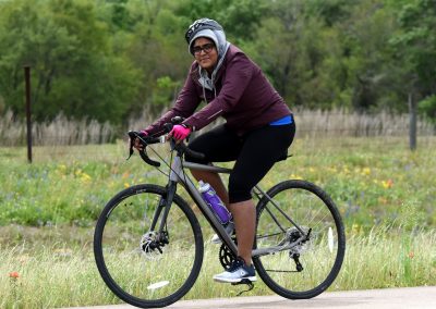 Vegan woman riding a bike on a scenic trail with lush greenery and wildflowers.
