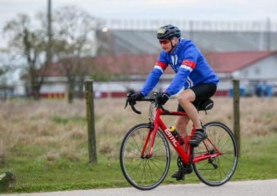 Bike rider wearing blue jacket and black shorts on red BMC road bike on a scenic trail.