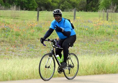 Vibrant cyclist riding through scenic wildflower field on Bluebonnet Express bike trail.