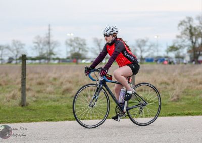High-performance road cyclist riding a bike on a paved trail during daytime, emphasizing fitness and active lifestyle.
