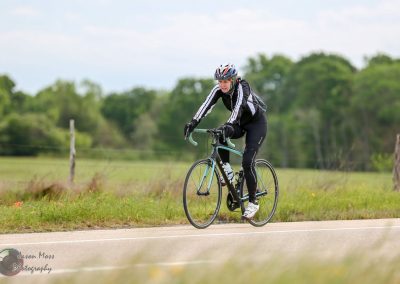 Cyclist riding a road bike on a scenic countryside road with green trees.