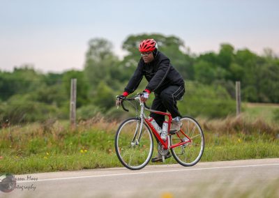 Bright red bicycle on scenic countryside bike route with cyclist wearing helmet and black sports apparel.