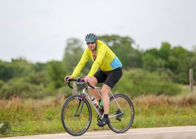 Bright yellow and blue cycling jacket worn by a man riding a road bike outdoors on a scenic route.