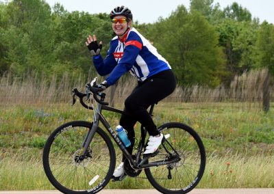 Bright smiling cyclist riding a black Masi bike on a scenic trail in Texas, promoting Bluebonnet Express cycling event.