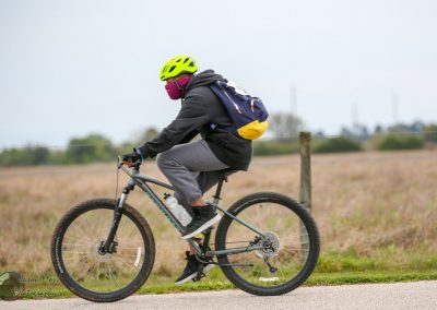 Bright yellow helmet and masked cyclist riding mountain bike on a paved trail.