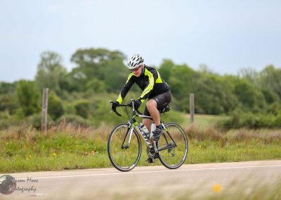 High-performance cyclist riding on scenic outdoor trail in a bright cycling jersey and helmet for Bluebonnet Express event.