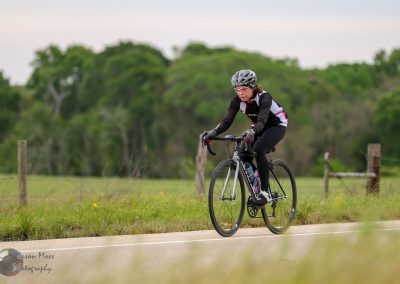 Quiet rural bike route with cyclist riding a black road bike through green fields, perfect for cycling enthusiasts.