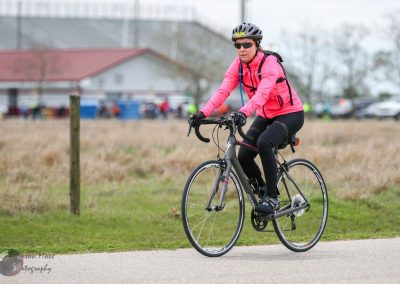 Vegan Biking woman in pink jacket and helmet riding a road bike outdoors.