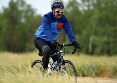 Vibrant cyclist riding in nature on a scenic trail during daytime with trees and greenery in the background.