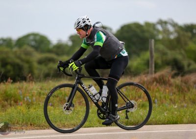 Versatile cyclist riding a Specialized road bike on a scenic rural route, promoting Bluebonnet Express bicycle services.