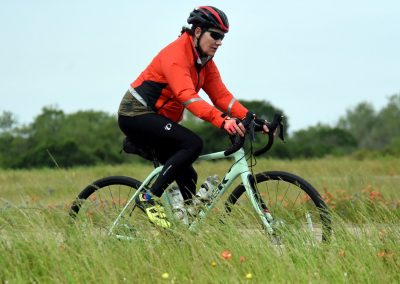 Bright red jacket cyclist riding through grassy field on Bluebonnet Express bike trail.