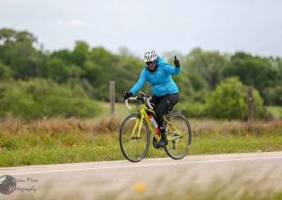 Bright cyclist in blue jacket riding Bluebonnet Express bike on scenic rural trail.