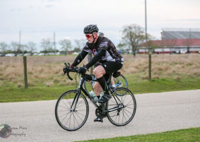 Cyclist riding a bike on a paved trail in a scenic outdoor setting with a rural background.