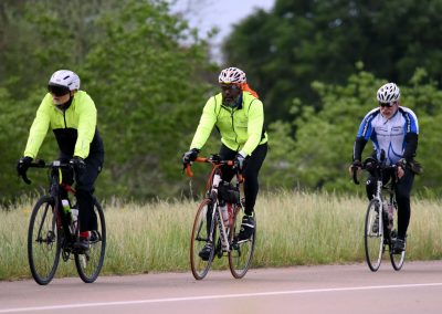 High-visibility cyclists riding on a scenic trail surrounded by greenery, promoting outdoor biking and fitness.