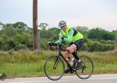 Bright green cycling jersey cyclist riding bike on scenic country road, smiling and waving.