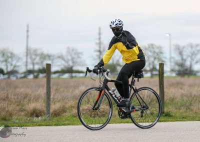 Cyclist wearing yellow jacket riding e-bike in outdoor park setting, showcasing Bluebonnet Express benefits.