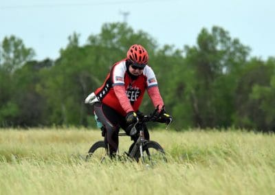 Guide bike rider in grassy field wearing helmet and cycling gear, promoting Bluebonnet Express bike tours.
