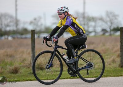 Elegant woman cycling on a road bike representing Bluebonnet Express event, outdoor cycling, fitness, and adventure.