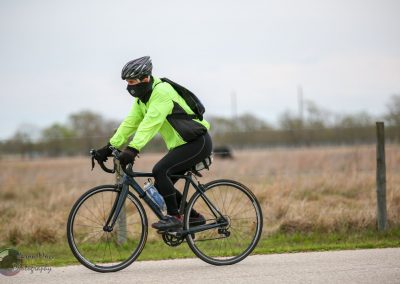 Bright green cycling jacket, black helmet, and mask on a touring bike in open countryside.