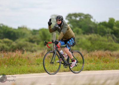 Vibrant cyclist riding on open road during daytime with lush greenery, promoting Bluebonnet Express bike services.