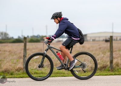 Vegan cyclist riding a mountain bike on a scenic trail with open fields and overcast sky.