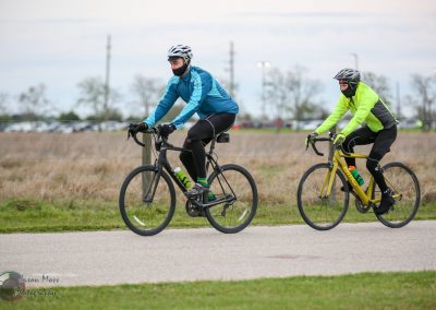 Sports cycling on a bike trail with two riders wearing helmets and high-visibility gear.