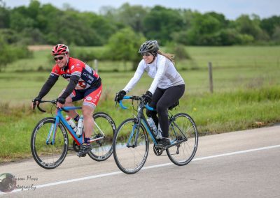 Bright blue and black women’s bikes with cyclists riding outdoors on a scenic rural road.