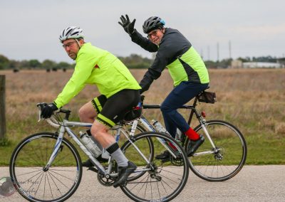 Bright yellow cycling jackets on two men riding bikes in outdoor countryside at dusk.