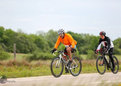Bright orange and black cycling jerseys on men riding bikes through scenic countryside.