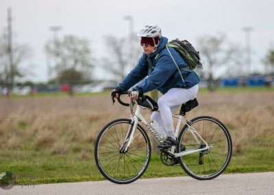 Comfortable woman riding hybrid bicycle on outdoor trail for Bluebonnet Express cycling event.