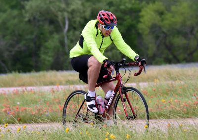 Vibrant cyclist riding a red bike on a scenic trail surrounded by wildflowers and greenery.